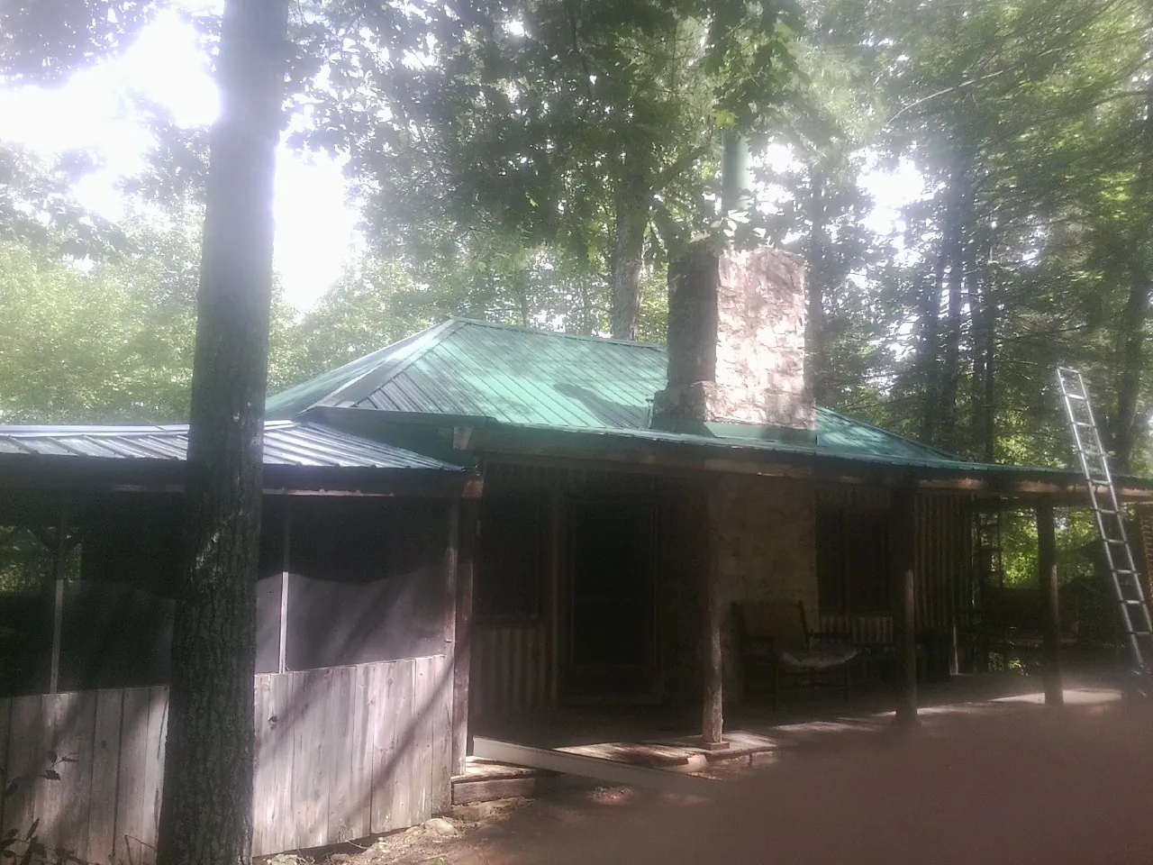 Green metal roof and stone chimney above a log cabin porch in Dover
